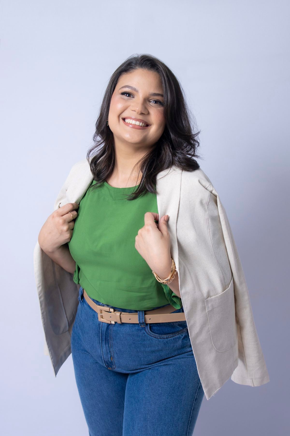 Maquiadora sorrindo de blusa verde e blazer bege nos ombros