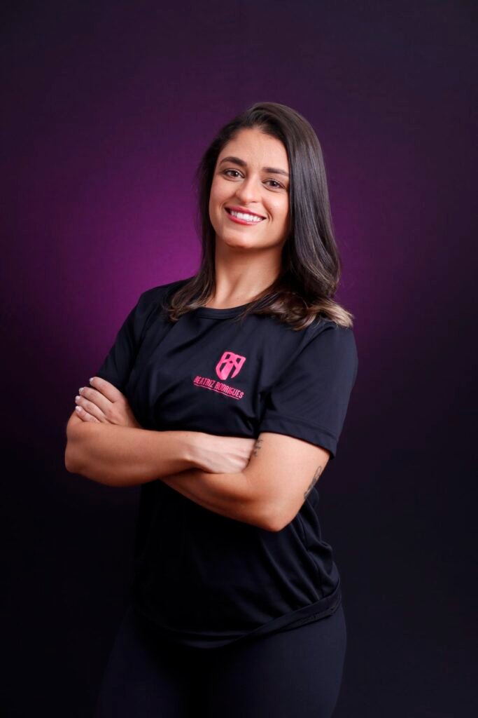 Personal trainer de camiseta preta e braços cruzados no fundo roxo do estúdio