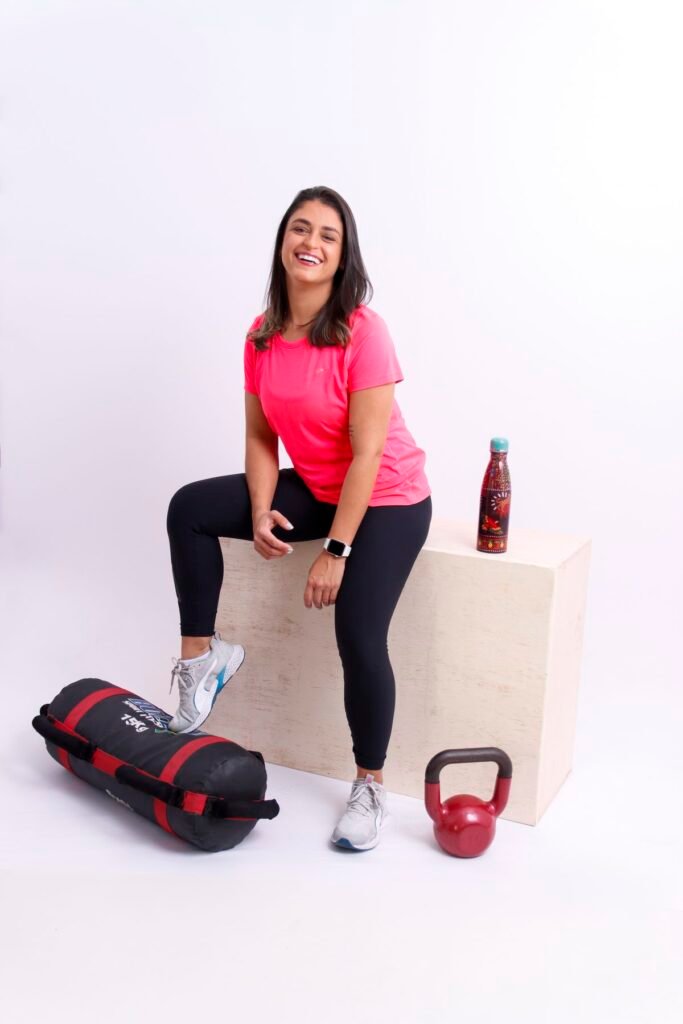Personal trainer sorrindo sentada na caixa de treino com kettlebell e saco de peso