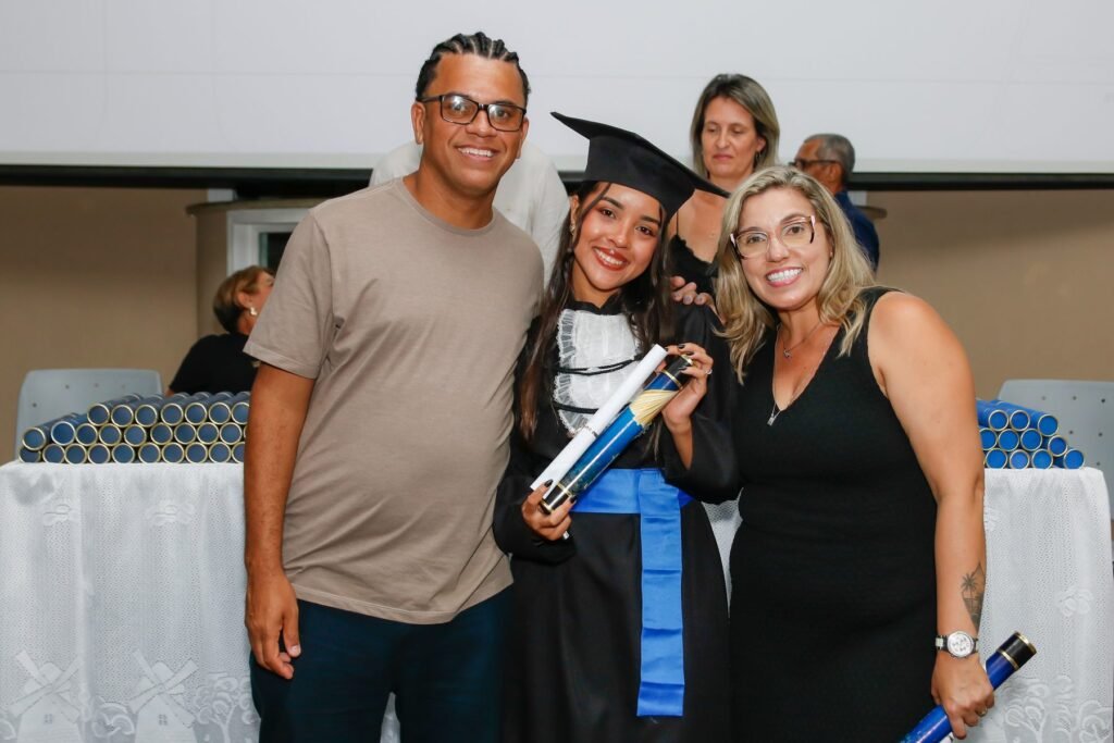 Formanda com o canudo ao lado de dois convidados depois da entrega do diploma