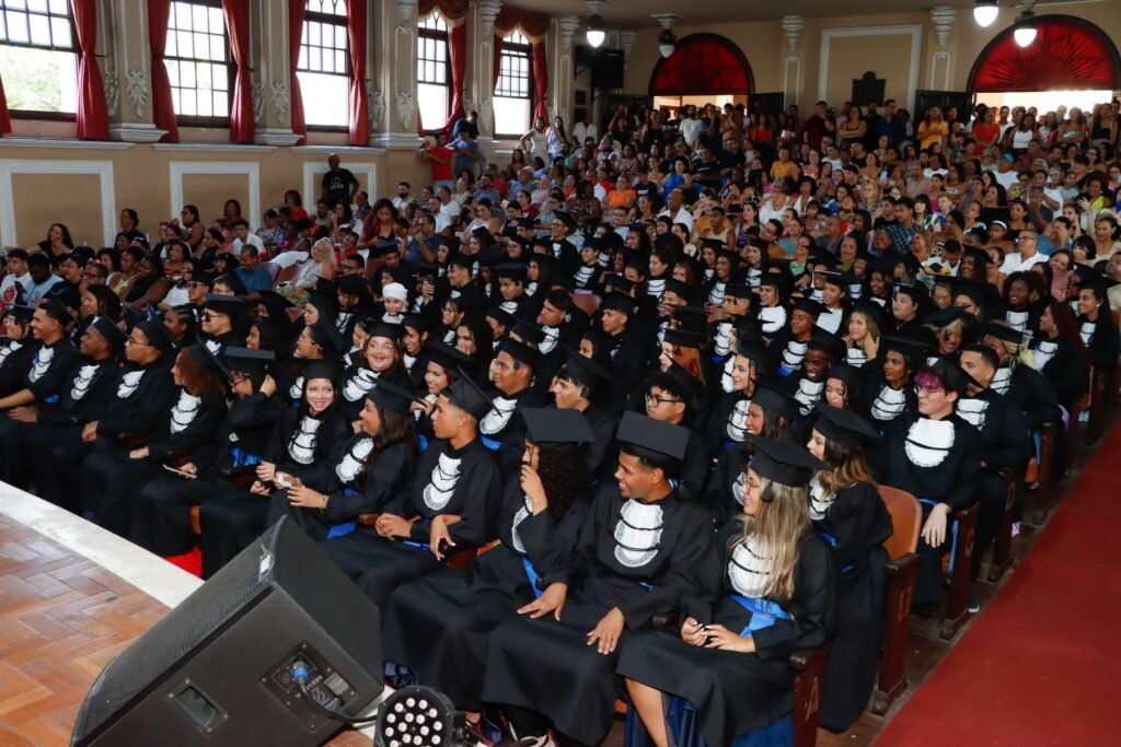 Formandos de beca e capelo sentados na plateia durante a colação de grau