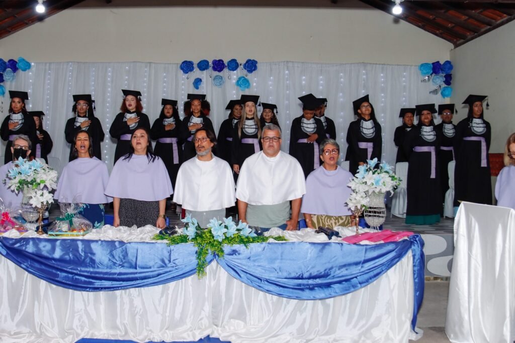 Mesa de honra e formandos cantando o hino na cerimônia de formatura