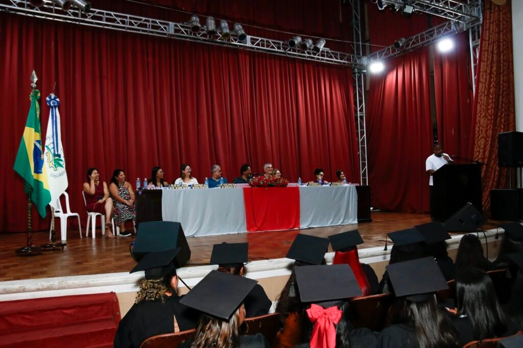 Mesa de honra e mestre de cerimônias no palco da colação de grau, com bandeiras ao lado